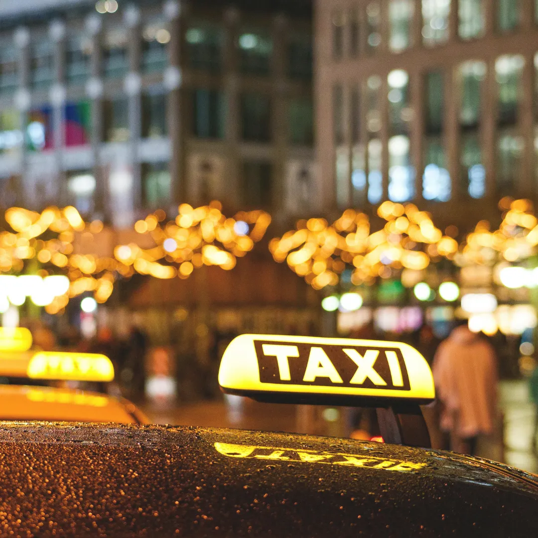 Φωτεινή επιγραφή TAXI σε όχημα τη νύχτα στην Αθήνα, με φόντο χριστουγεννιάτικα φώτα. Η μίσθωση minibus είναι καλύτερη εναλλακτική για γκρουπ.