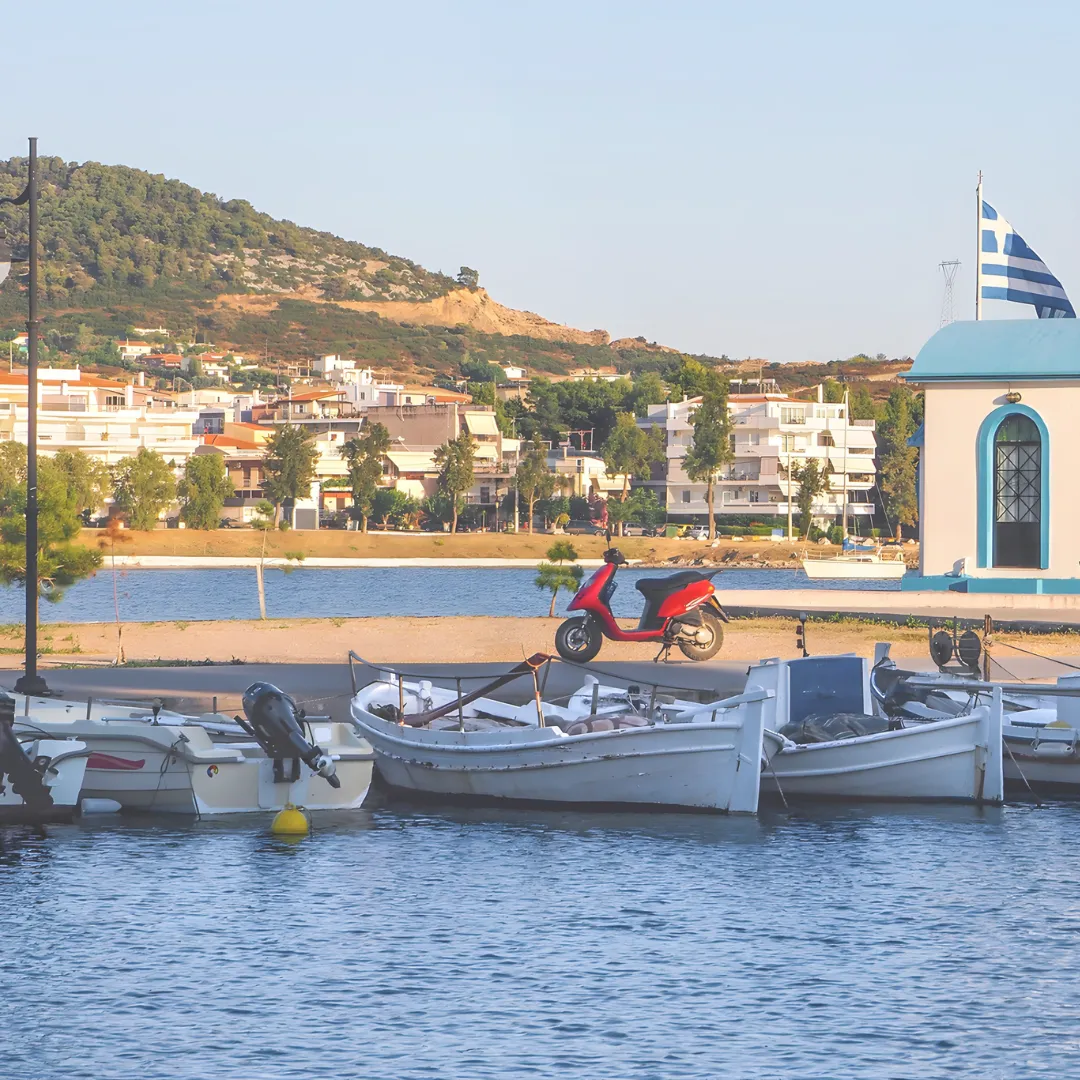 Γραφικό λιμανάκι με βάρκες και την ελληνική σημαία, ιδανική στάση για φαγητό και βόλτα με VIP Minibus.